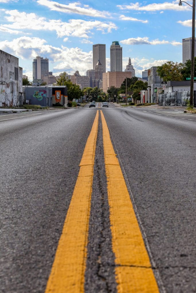 Two rich yellow lines trace down the middle of a bitumen road. Tulsa’s city skyline rises in the background. There’s a feeling of a small town having grown into a city.