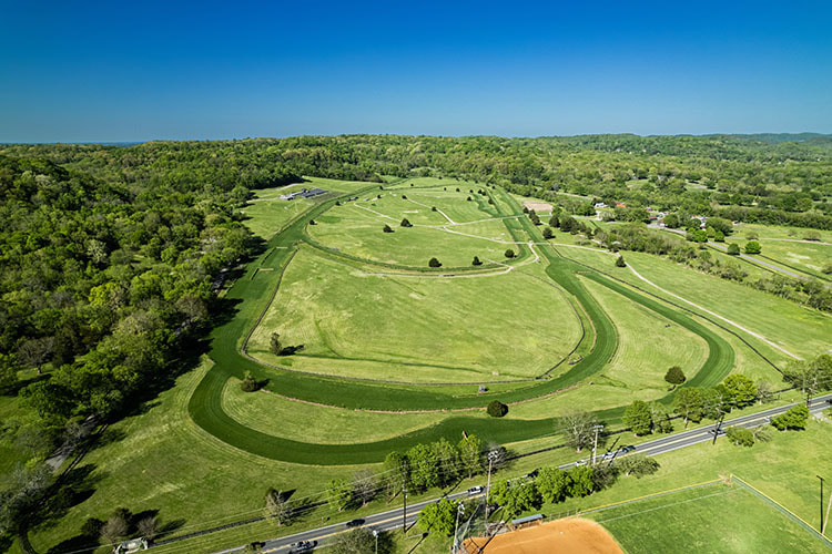 A large tract of vibrant green land with only a few distantly separated buildings on it. 